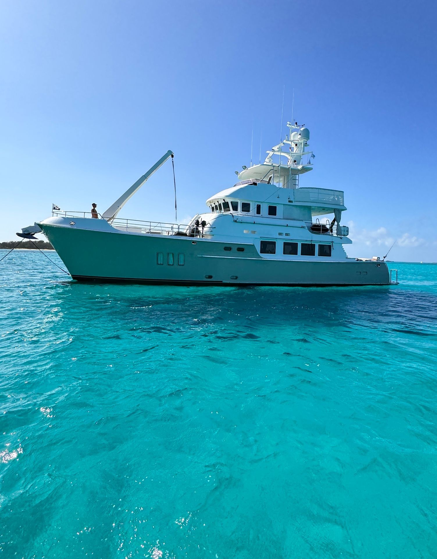 Large white yacht anchored in clear turquoise waters under a bright blue sky.