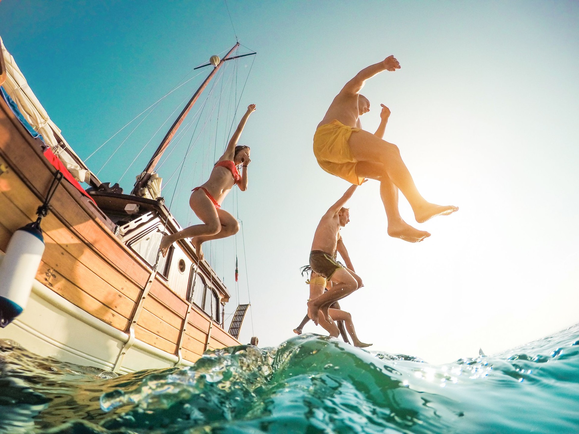 Happy friends diving from sailing boat into the sea - Young people jumping inside ocean in summer excursion day - Vacation, youth and fun concept - Main focus on left man - Fisheye lens distortion