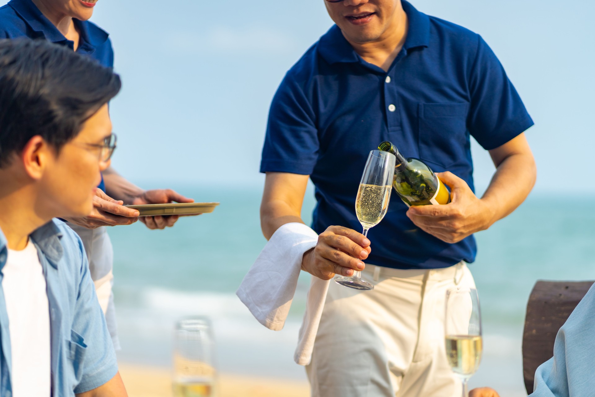 Waiter and waitress serving champagne to customers at beach restaurant.